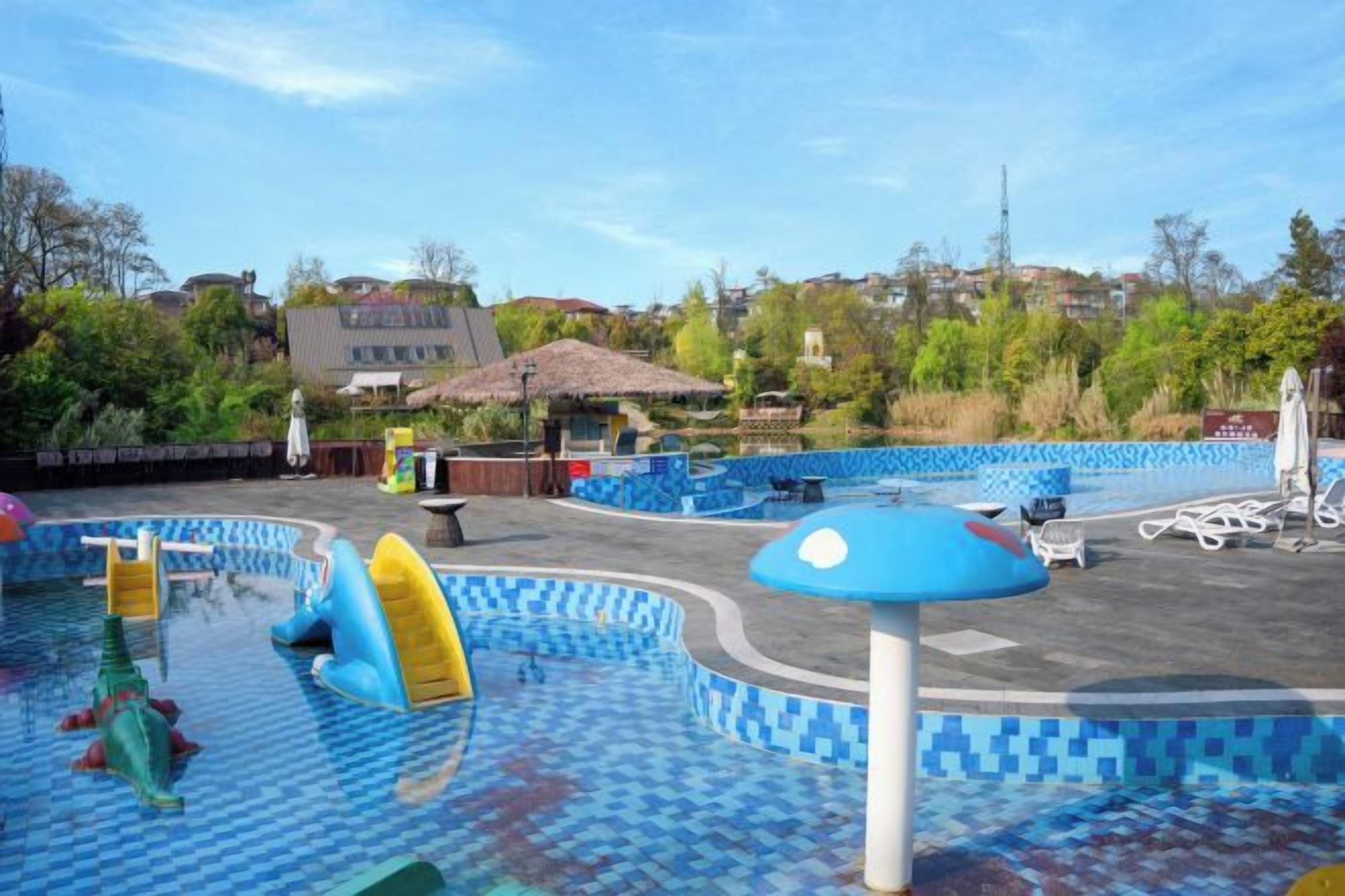 A water park with multiple pools and play areas, surrounded by greenery and a clear sky.