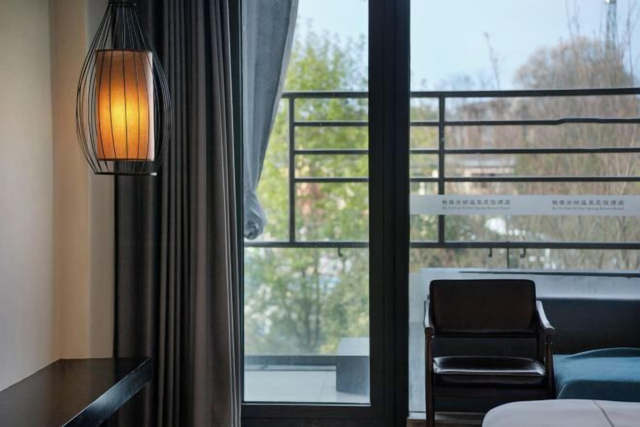 Ein Zimmer mit großem Fenster, schwarzem Sessel, einer Couch und einer Wandlampe.