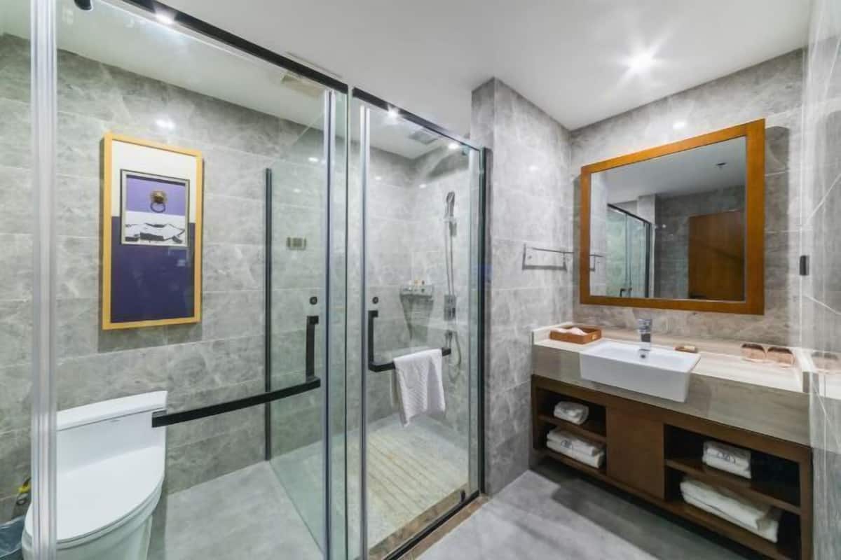 Een moderne badkamer met een douchecabine van glas, een grote spiegel en een wand betegeld met marmer.