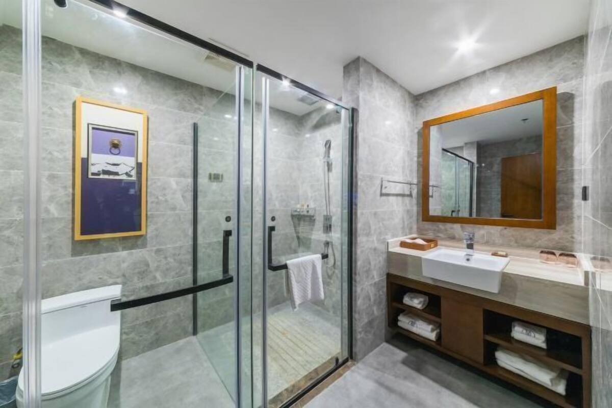 Un baño moderno con ducha de vidrio, un espejo grande y pared de azulejos de mármol.