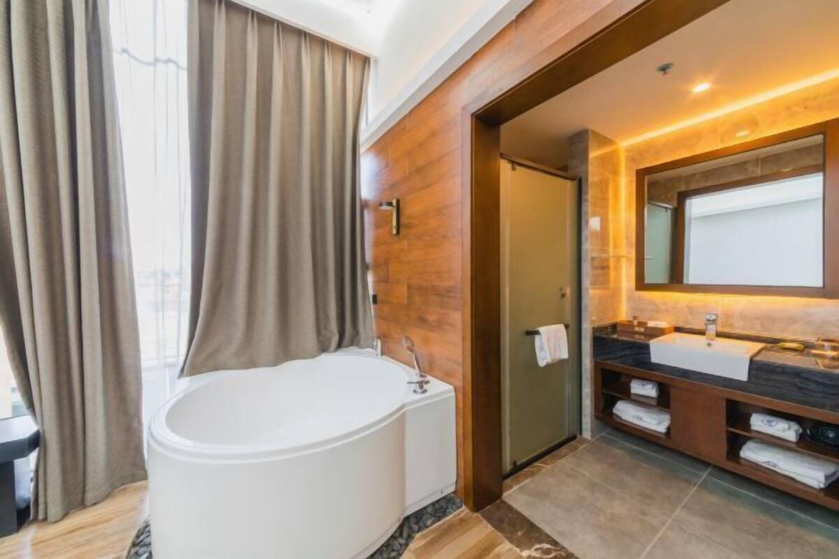Un baño moderno con una bañera independiente, un espejo grande y un tocador con lavabo y espacio para toallas.