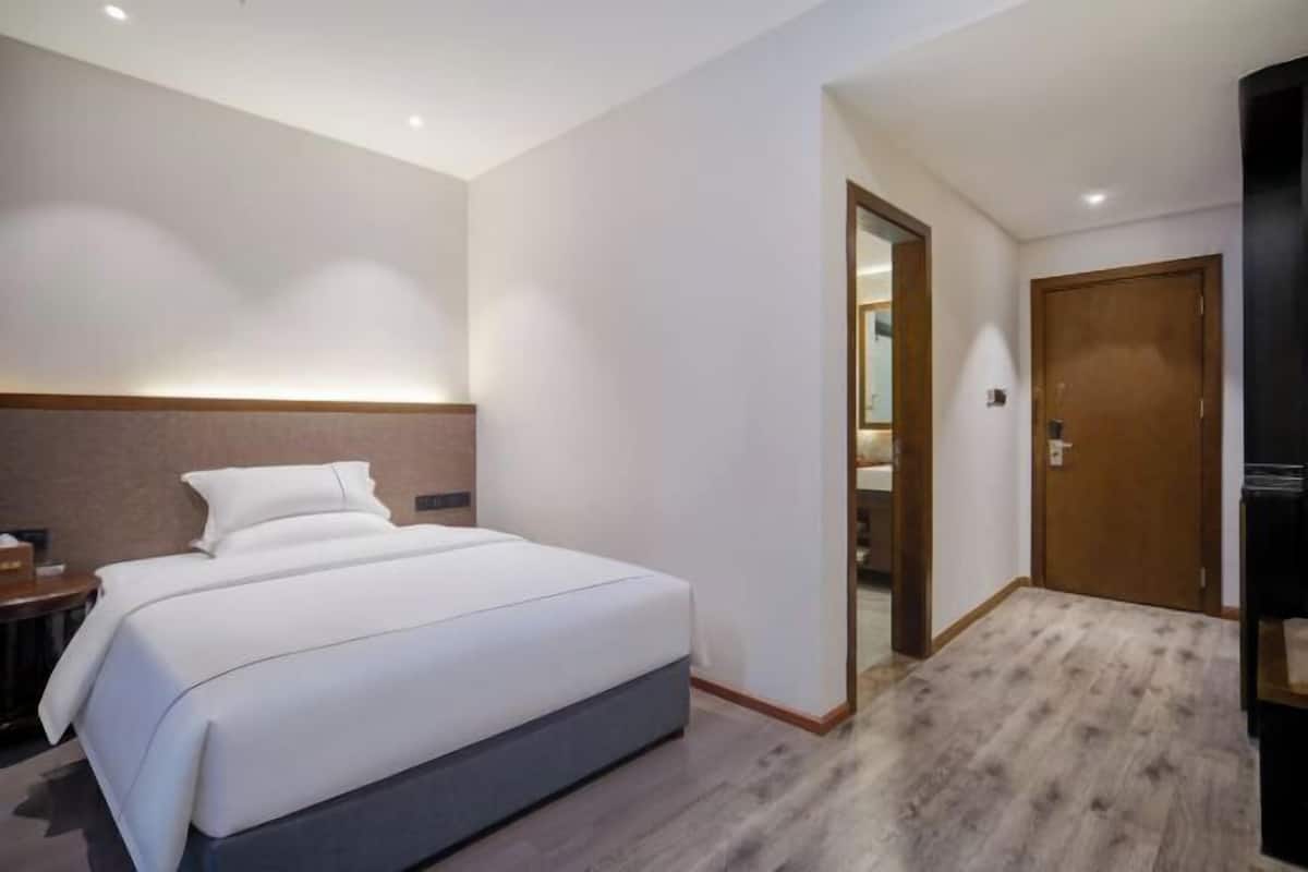Een hotelkamer met een bed, een houten hoofdeinde, een nachtkastje en een deur die naar een andere kamer leidt.