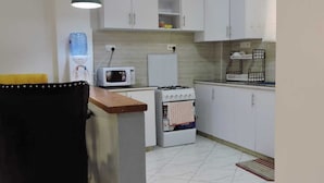 A compact kitchen with white cabinets, a microwave, a stove, and a water dispenser. - Nanyuki One Bedroom Apartment (Nanyuki)
