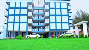 A multi-story building with a central atrium, several balconies, and a parking area with cars. - Nanyuki One Bedroom Apartment (Nanyuki)