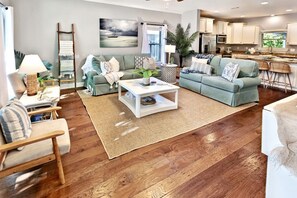 A modern living room with a sofa set, a coffee table, and a kitchen in the background.