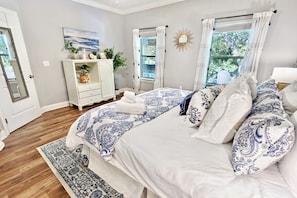 A bedroom with a large bed, a dresser, a mirror, and a window with curtains.