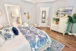 A bedroom with a bed, bedside tables, a dresser, a mirror, a door, and a wall-mounted artwork.