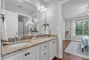 A bathroom with a double sink, white cabinets, a large mirror, and a potted plant.