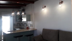 Cozinha moderna com ilha central, luminárias pendentes e um sofá numa sala de estar.