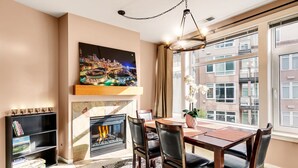 Un área de comedor con chimenea, un ventanal con vista a la ciudad y una estantería llena de libros.
