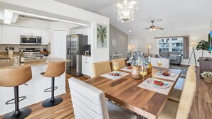 Una cocina moderna con armarios blancos, un refrigerador de acero inoxidable y un comedor con mesa de madera y taburetes de bar.