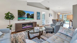 Una sala de estar moderna con un televisor de pantalla plana, asientos cómodos, una mesa de centro de vidrio y un ventanal con vistas al exterior.