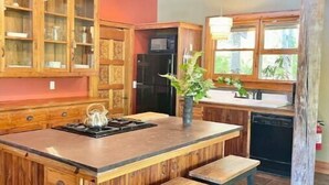 A kitchen with wooden cabinetry, a central island with stools, and a refrigerator. - Unique Cypress cottage, close to Charlottesville with mountain views. (Charlottesville)