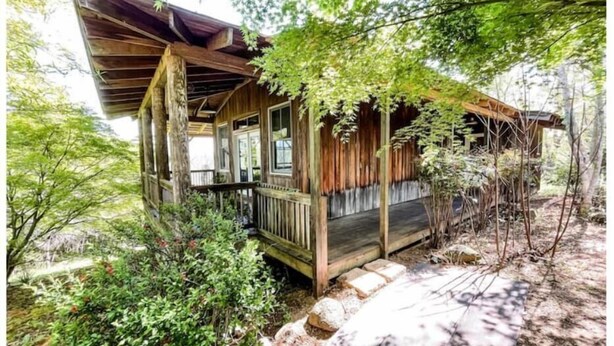 A rustic wooden cabin with a porch, surrounded by dense foliage and a stone pathway. - Unique Cypress cottage, close to Charlottesville with mountain views. (Charlottesville)
