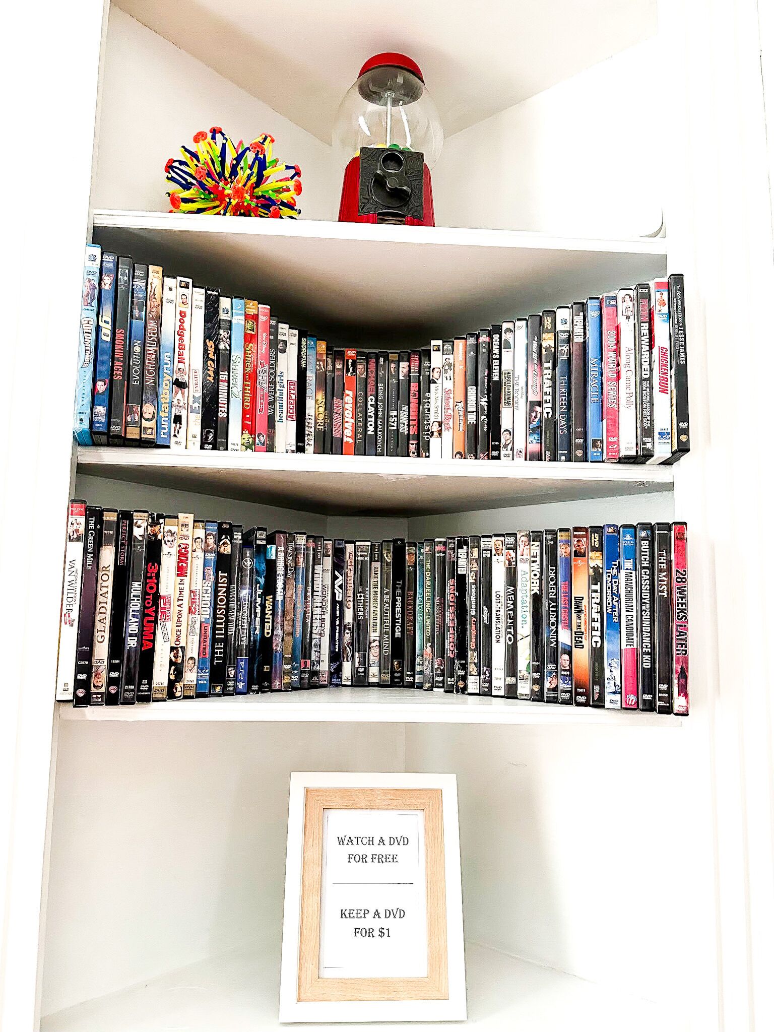 Una estantería con DVD y un cartel enmarcado que ofrece DVD gratis o por 1 dólar.