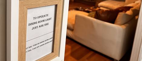 A digital clock on a wall displaying the time as 7:43. Below it, there is a framed sign instructing to ask the maid to turn on the dining room light.