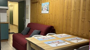 Una habitación acogedora con pared de madera, un sofá rojo, una mesa de comedor de madera con individuales, y una cocina al fondo.
