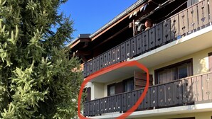 Un edificio de dos pisos con balcones, un gran árbol de hoja perenne y un césped bien cuidado.
