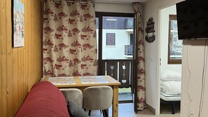 Una habitación acogedora con un sofá rojo, una mesa de madera y un televisor montado en la pared.