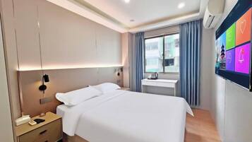 A modern hotel room with a bed, bedside table, and a digital display on the wall.