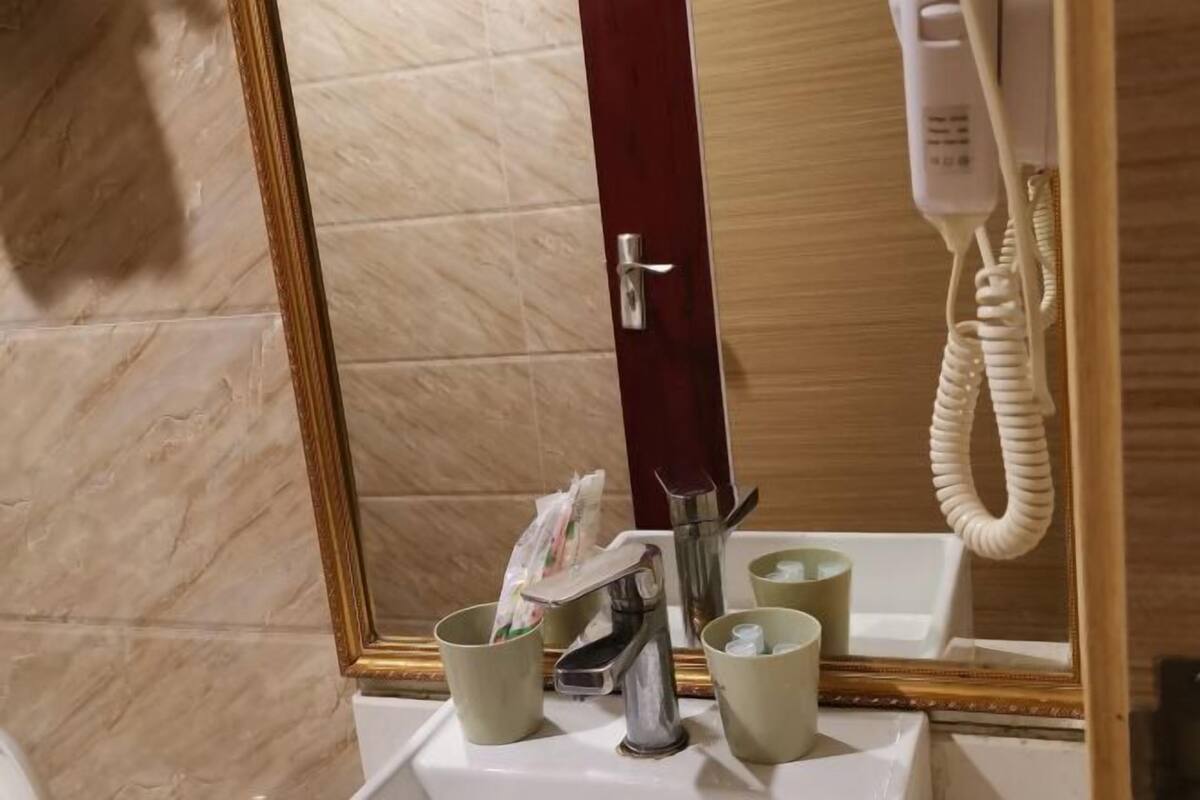 Um banheiro com piso de mármore, espelho com moldura dourada, pia branca e telefone.