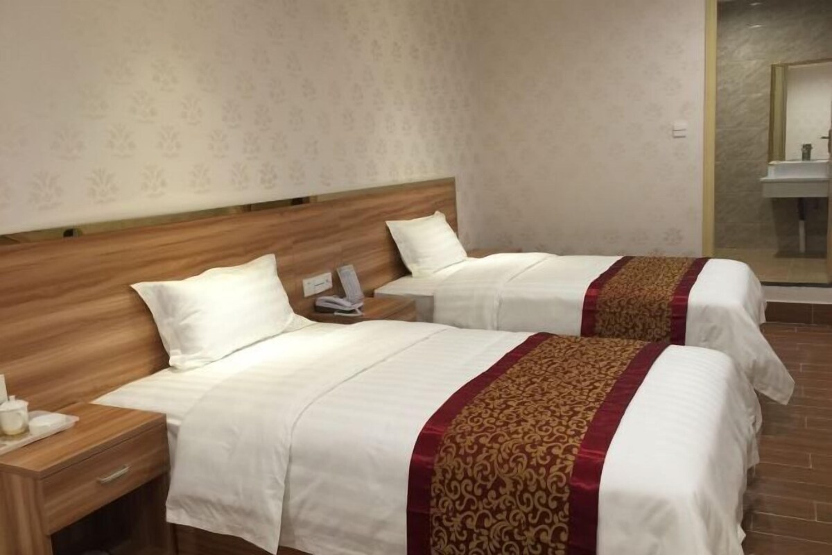 A hotel room with two beds, wooden headboards, white bedding, and a red and gold decorative trim.