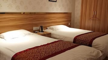 Duas camas de solteiro com lençóis brancos e detalhes vermelhos decorativos, uma cabeceira de madeira, uma mesa de cabeceira com luminária e um cabideiro.