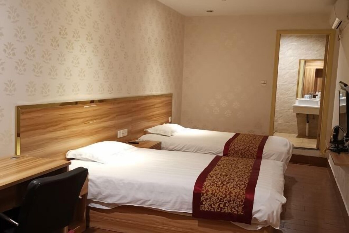 A hotel room with two beds, a wooden headboard, a desk with a chair, and a mirror.