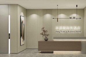 A reception area with a reception desk, a vase with flowers, and a wall-mounted sign. - Fengyuanju Business Hotel (Zhongshan)