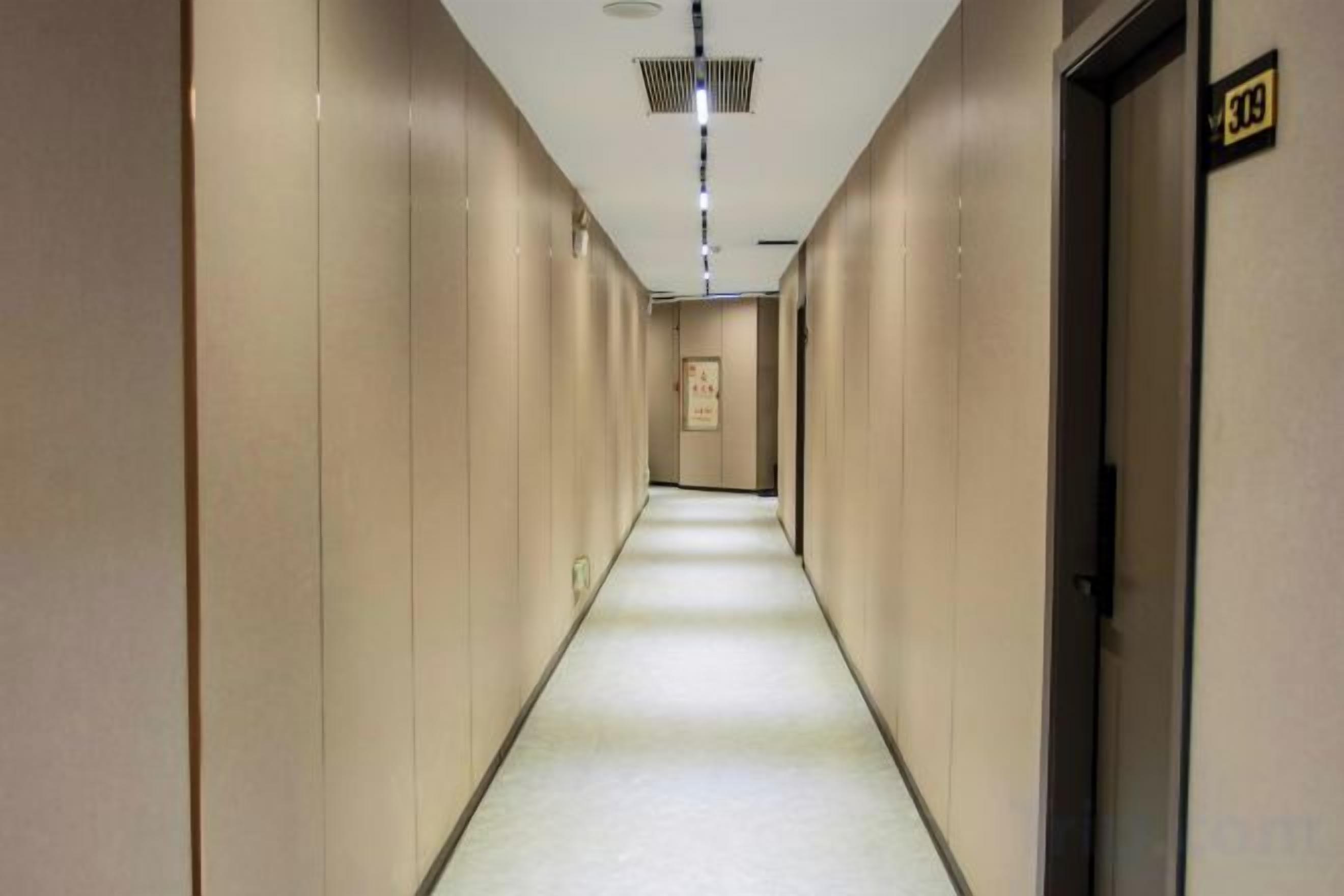 A hotel hallway with a carpeted floor, doors on the right, and a sign above the doors.