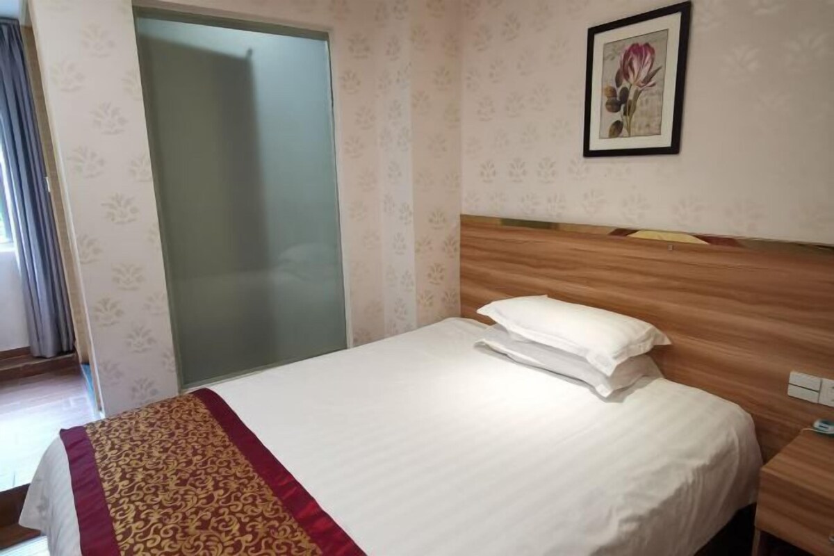 A hotel room with a bed, a wooden headboard, a framed picture on the wall, and a door with a frosted glass panel.