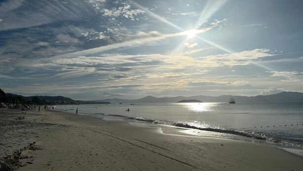 A beach with a clear sky, calm sea, and distant mountains. - Ilha Forte Praia Hotel (Florianópolis)