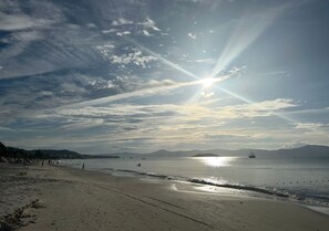 Una playa con cielo despejado, mar tranquilo y montañas a lo lejos.