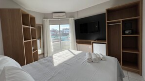 A hotel room with a large bed, a TV mounted on the wall, a wardrobe, and a balcony with curtains. - Ilha Forte Praia Hotel (Florianópolis)
