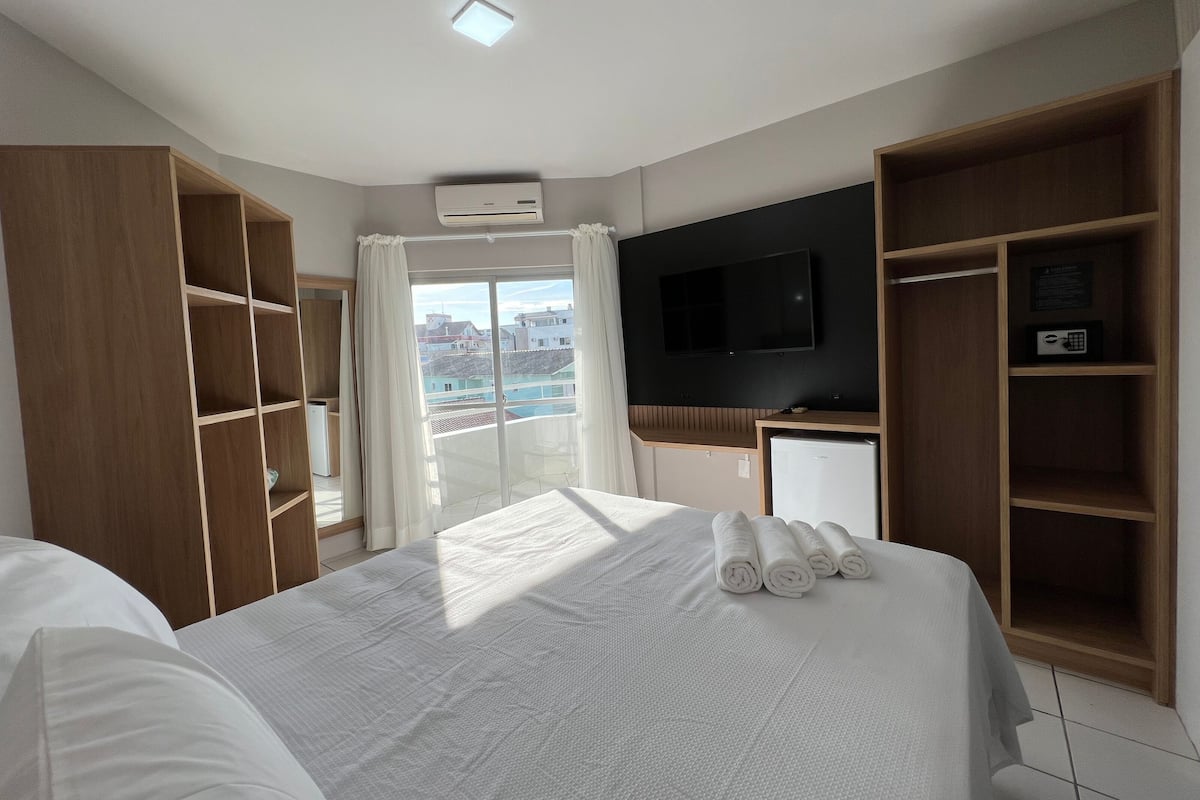 A hotel room with a large bed, a TV mounted on the wall, a wardrobe, and a balcony with curtains.