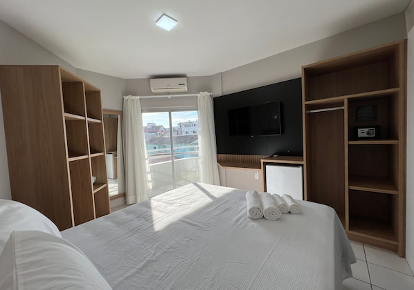 A hotel room with a large bed, a TV mounted on the wall, a wardrobe, and a balcony with curtains. - Ilha Forte Praia Hotel (Florianópolis)