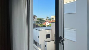 A view through a window with a door, revealing a building with a red roof and white walls. - Ilha Forte Praia Hotel (Florianópolis)