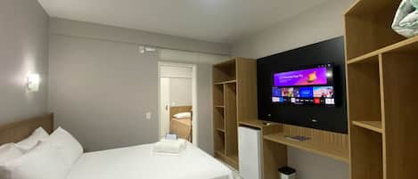A hotel room with a bed, a TV mounted on the wall, a desk, and a small refrigerator.