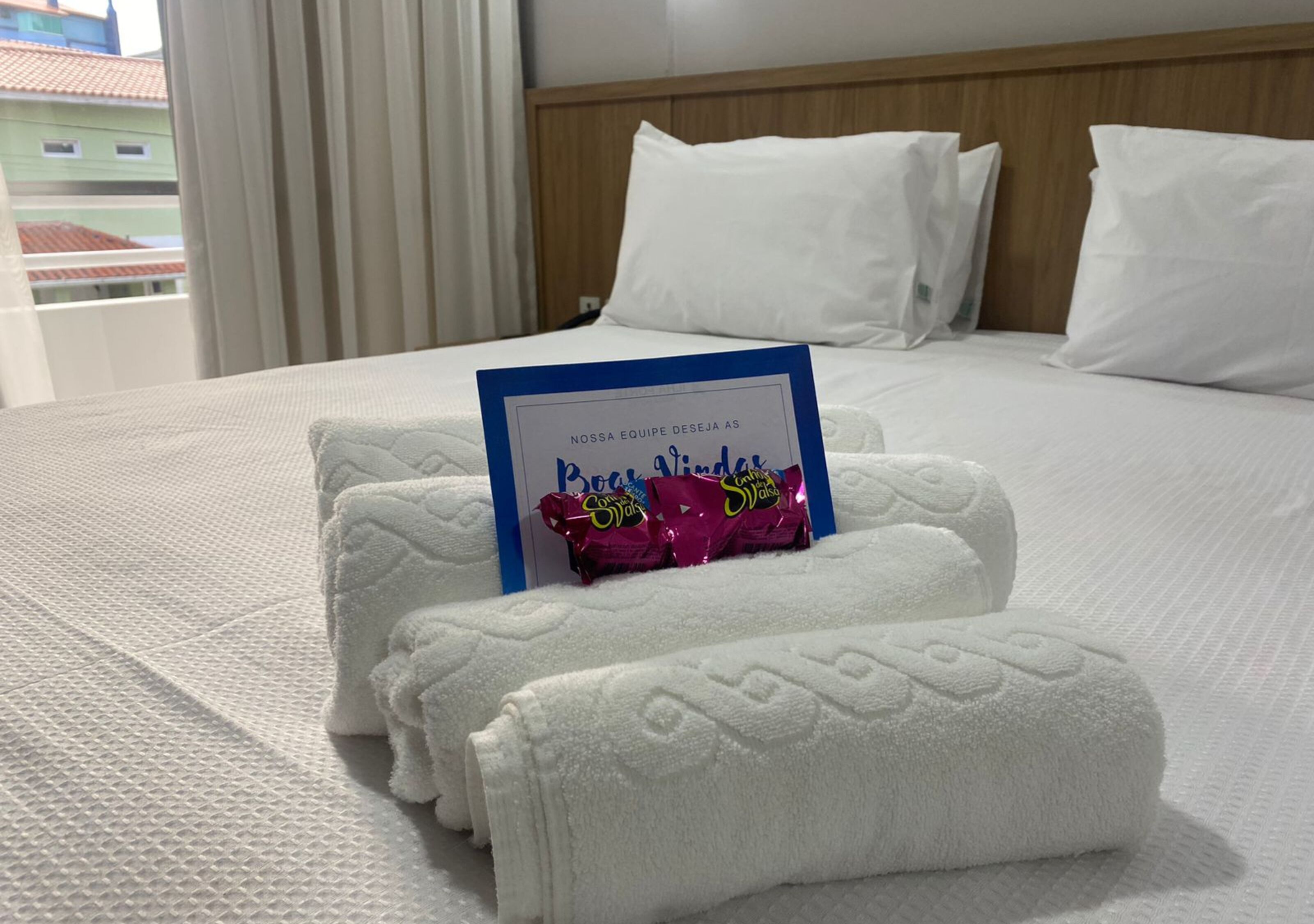 A neatly made bed with white linens, a blue sign with text, and a pair of white towels.