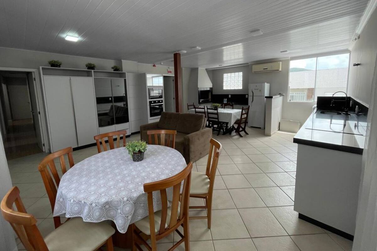 A compact kitchen with a dining area, featuring a round table with a lace tablecloth, wooden chairs, and a sofa.