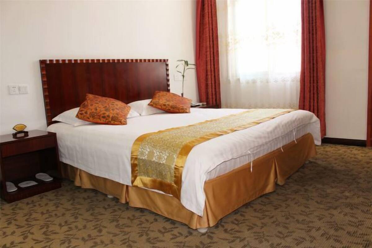 Une chambre d’hôtel avec un grand lit, une table de chevet, une lampe et une fenêtre avec des rideaux.