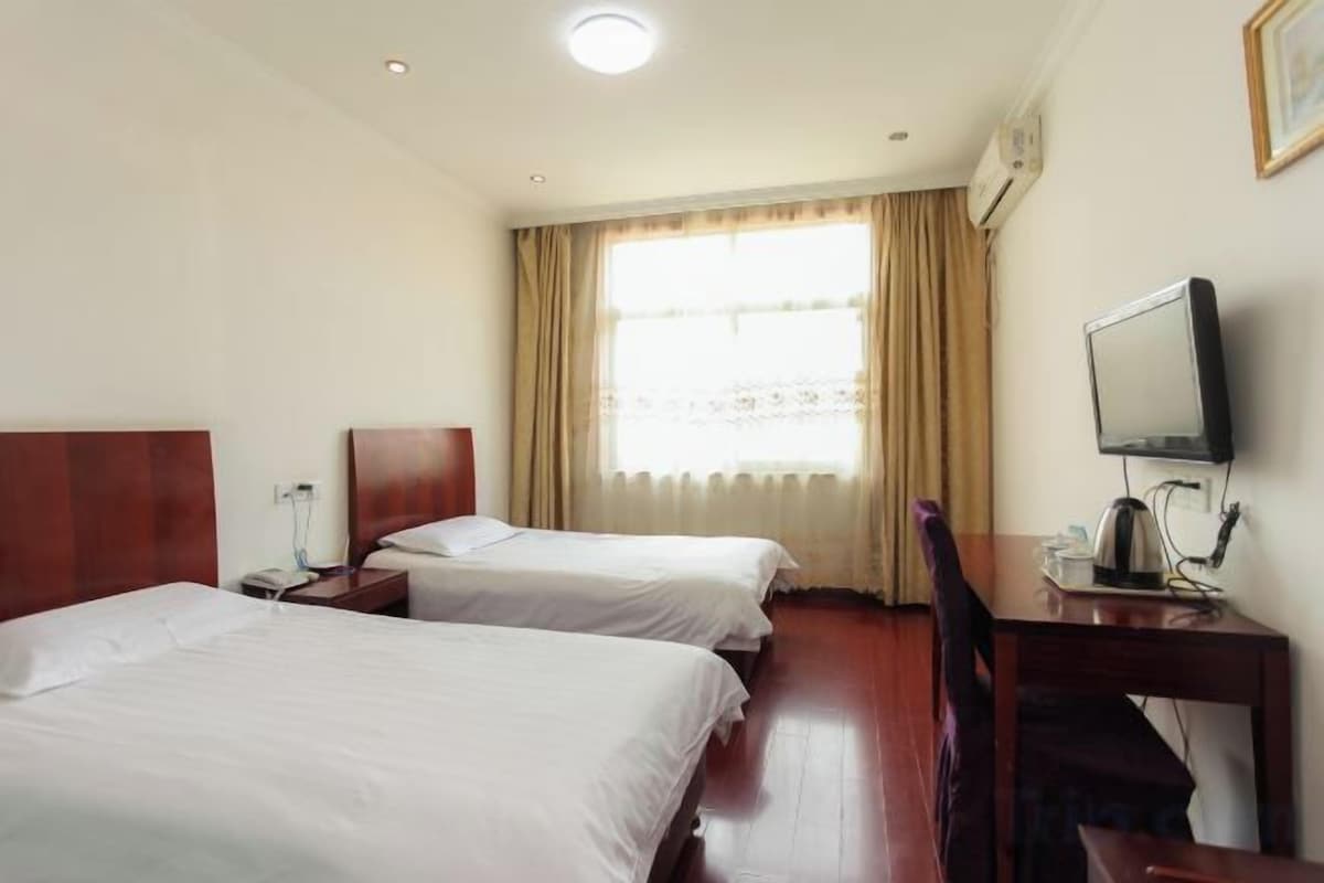 A hotel room with two beds, a desk with a computer, and a window with curtains.