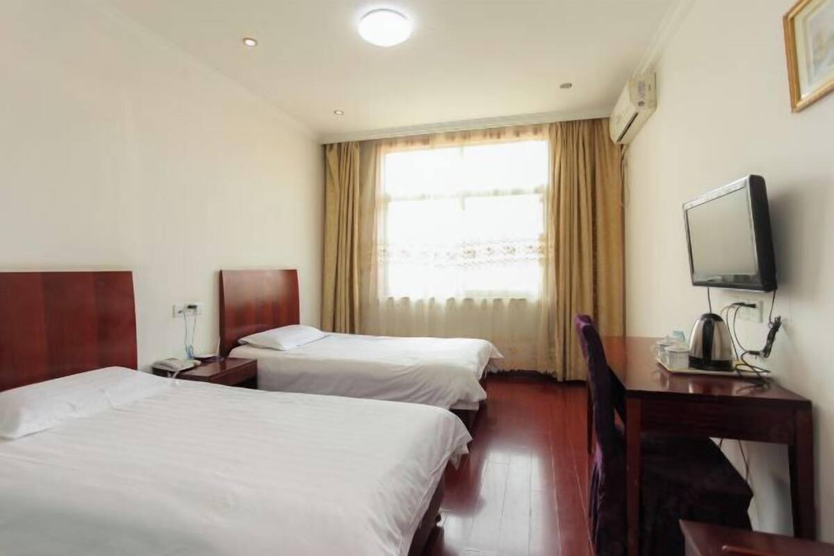 Une chambre d’hôtel avec deux lits, un bureau avec une chaise, une télévision et une fenêtre avec des rideaux.