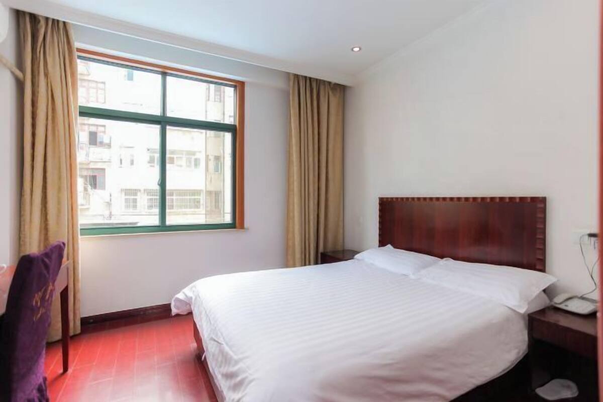 Une chambre d’hôtel avec un grand lit, une tête de lit en bois, une fenêtre avec des rideaux et un bureau avec un téléphone.
