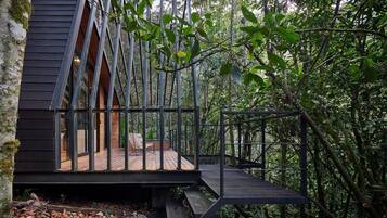 Una cabaña de madera moderna con balcón de cristal, rodeada de un bosque denso.