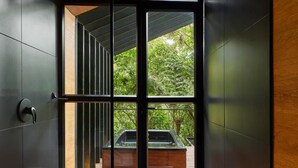 Interior modern amb sostre de fusta, una porta de vidre que dona a un espai exterior, i una vista de verdura i un cotxe a l'exterior.