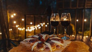 Una taula de fusta amb una safata de tast de carn i dues copes de vi vermell, amb un fons de llums borroses.