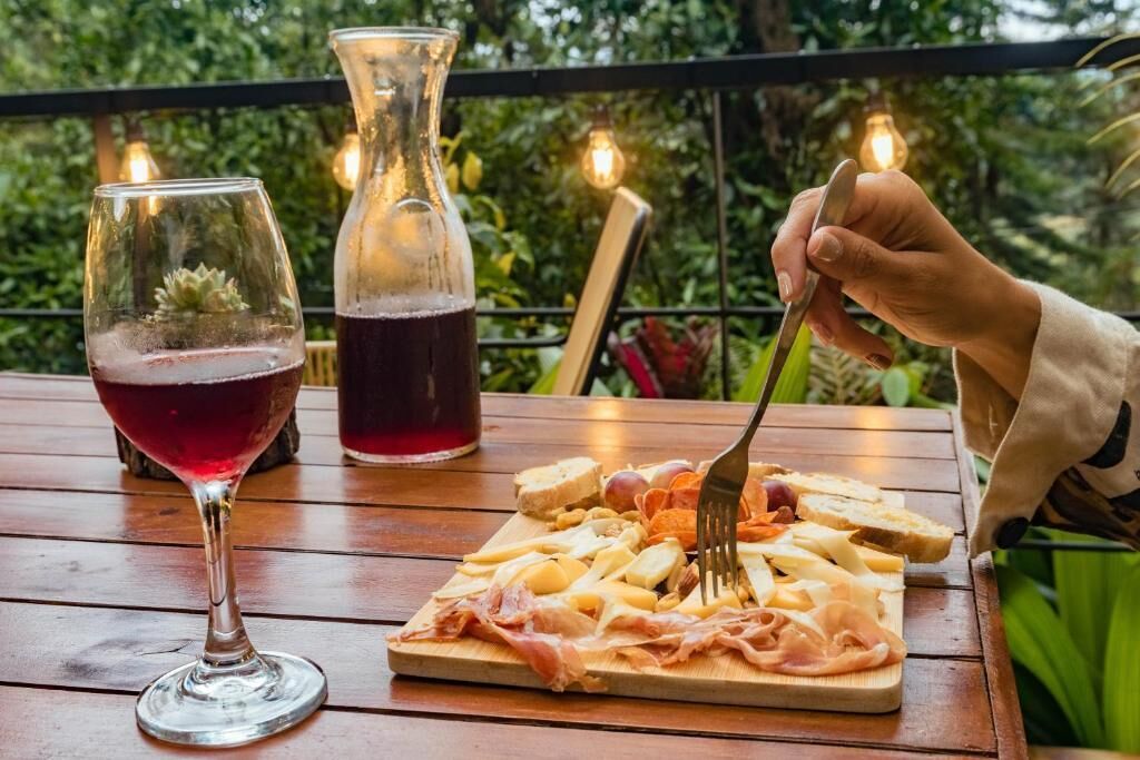 A wooden table with a charcuterie board, a glass of red wine, and a bottle of red wine.