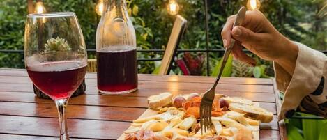 A wooden table with a charcuterie board, a glass of red wine, and a bottle of red wine.