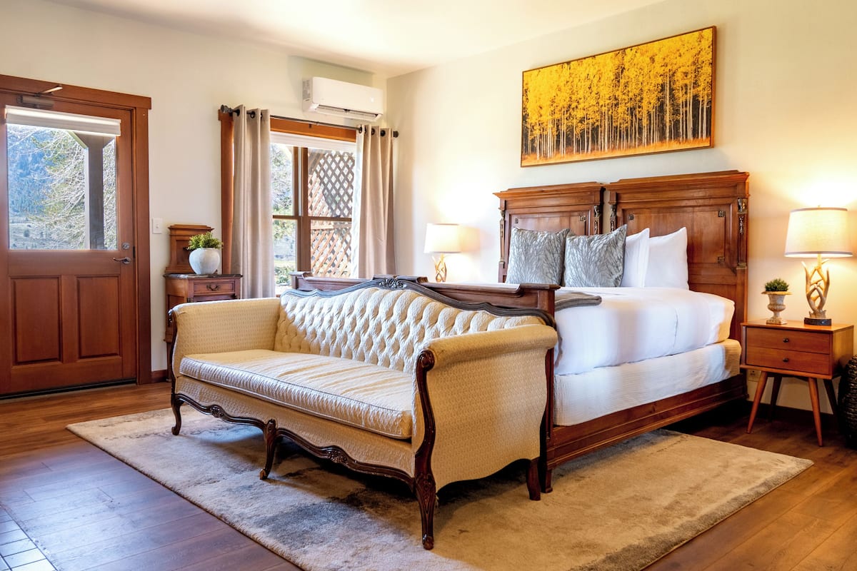 A bedroom with a large bed, a sofa, a wooden nightstand, a lamp, and a painting on the wall.